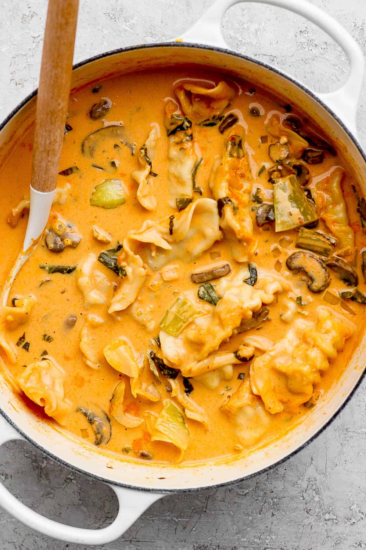 Bok choy and mushrooms added to a pot of potsticker soup with a ladle sticking out the side.