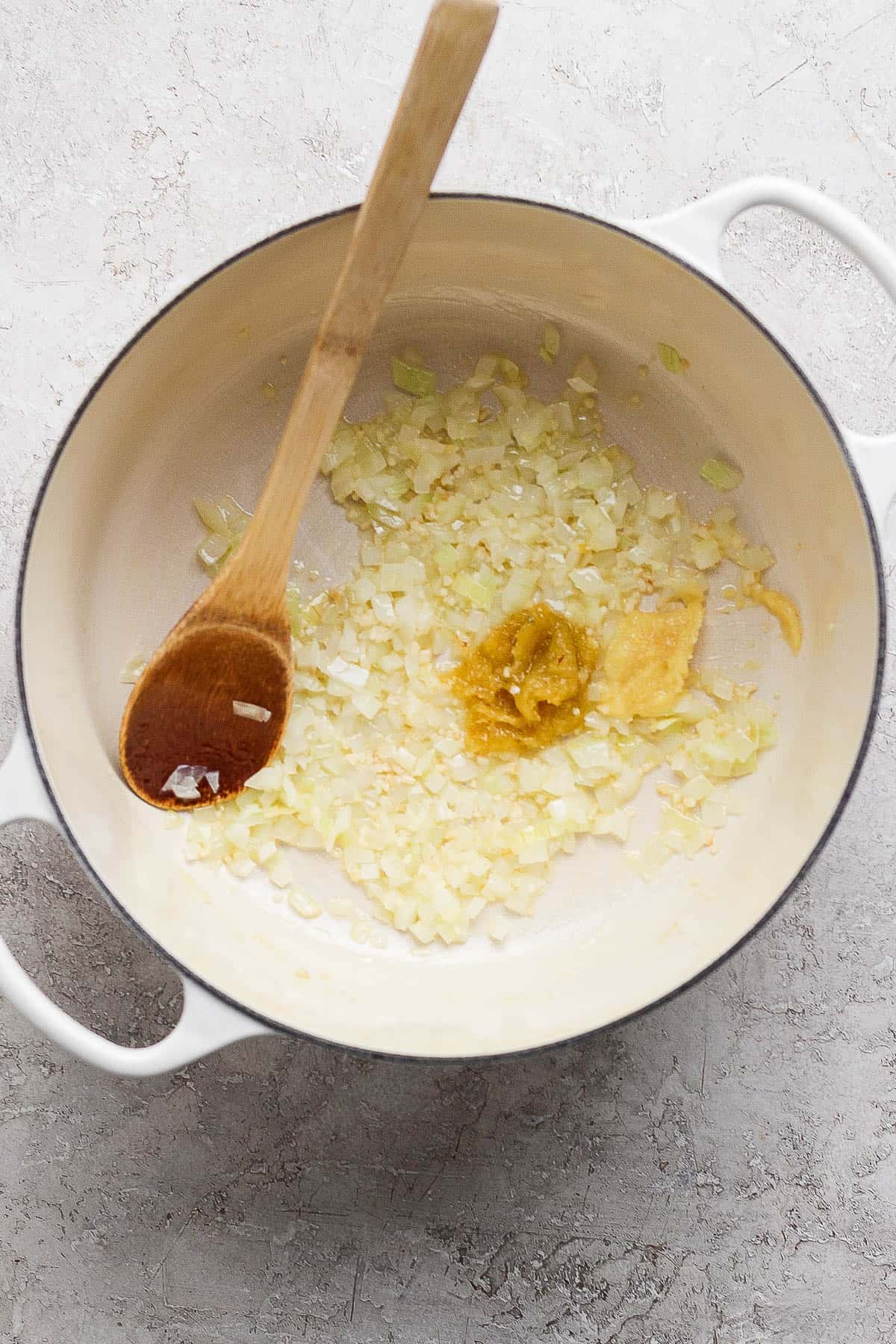 Onion, garlic, lemongrass, and garlic sautéing in a pot with a wooden spoon.