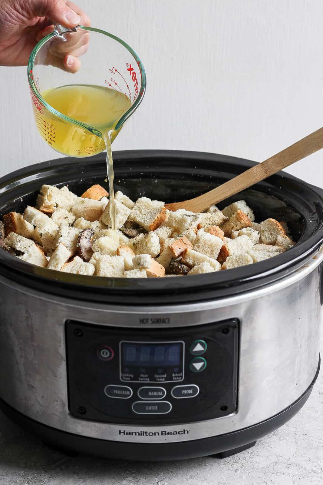 A hand pouring chicken broth into the crock pot stuffing.