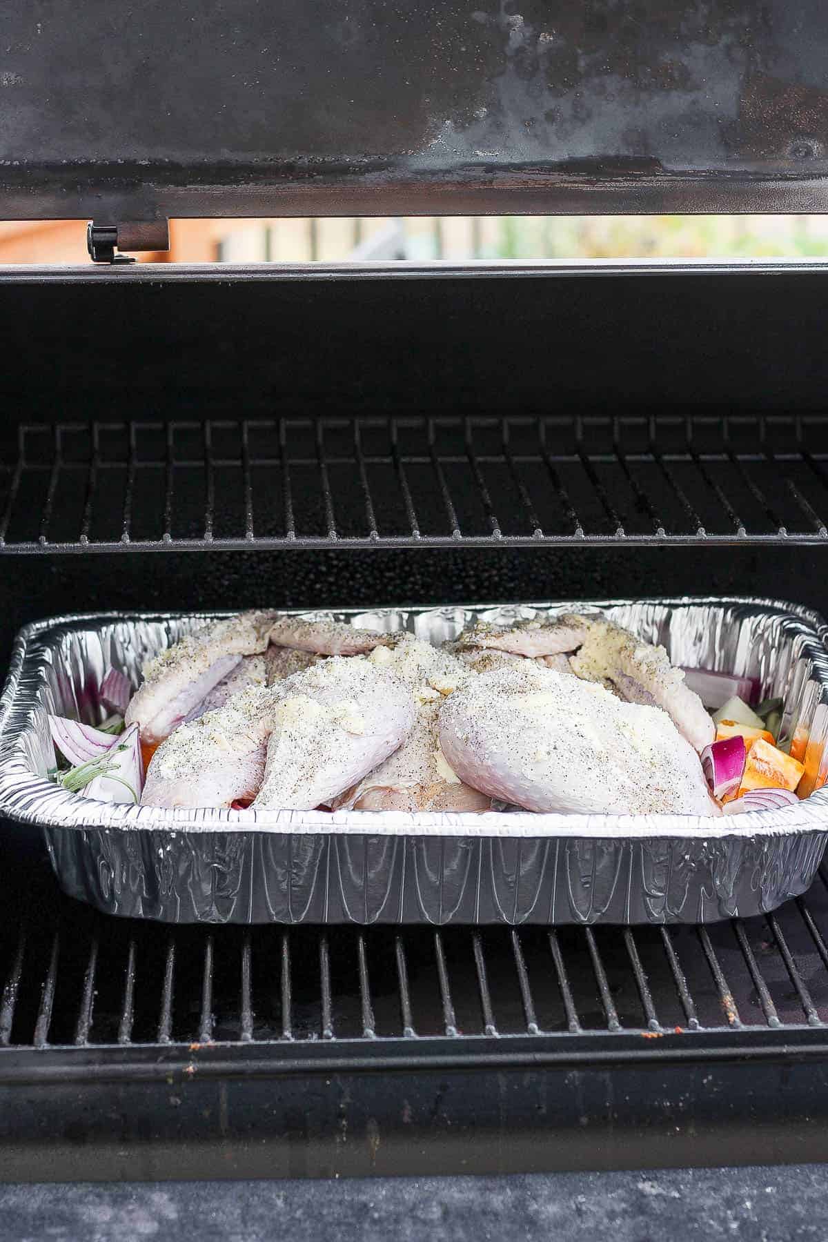 A seasoned spatchcock turkey in a roasting pan on the grates of a smoker.