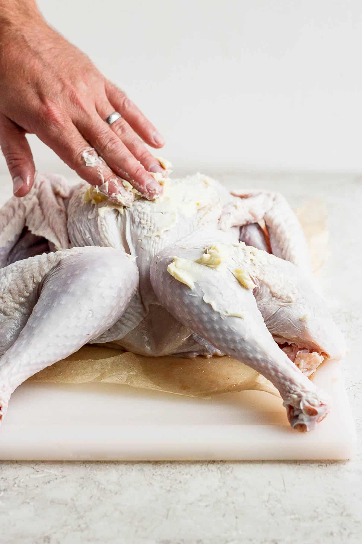 Soft butter being rubbed on the outside of a spatchcock turkey.