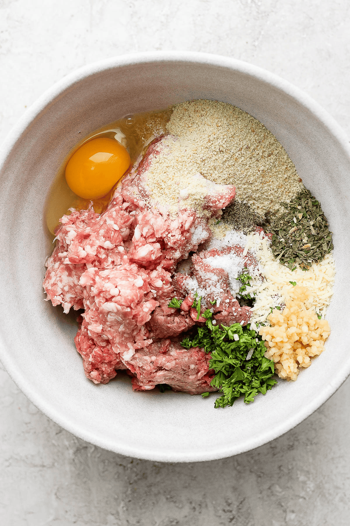 Ingredients for the meatballs in Italian wedding soup separated in a mixing bowl.