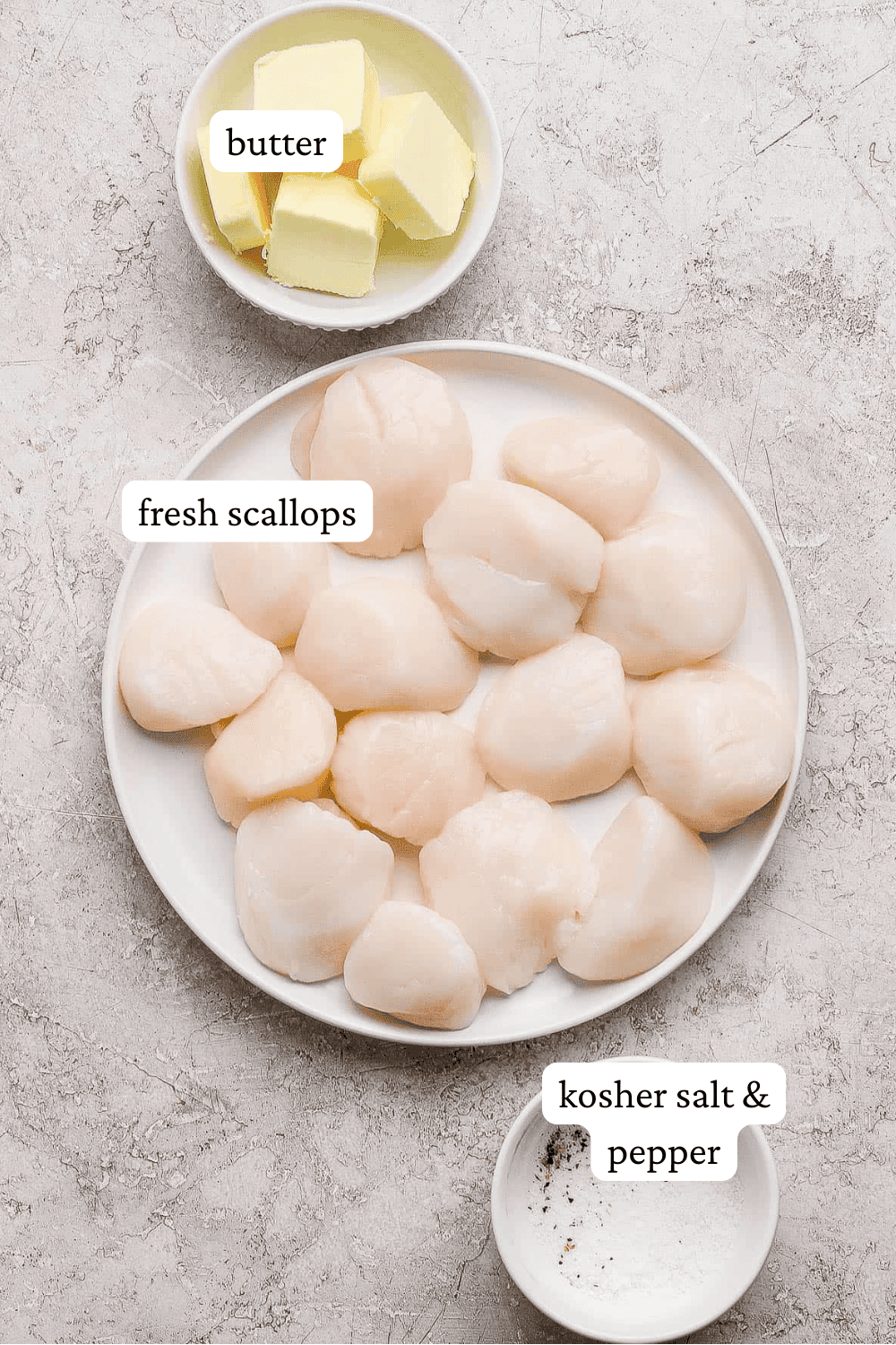 Several scallops on a white plate next to a bowl of butter and a small bowl of salt and pepper.