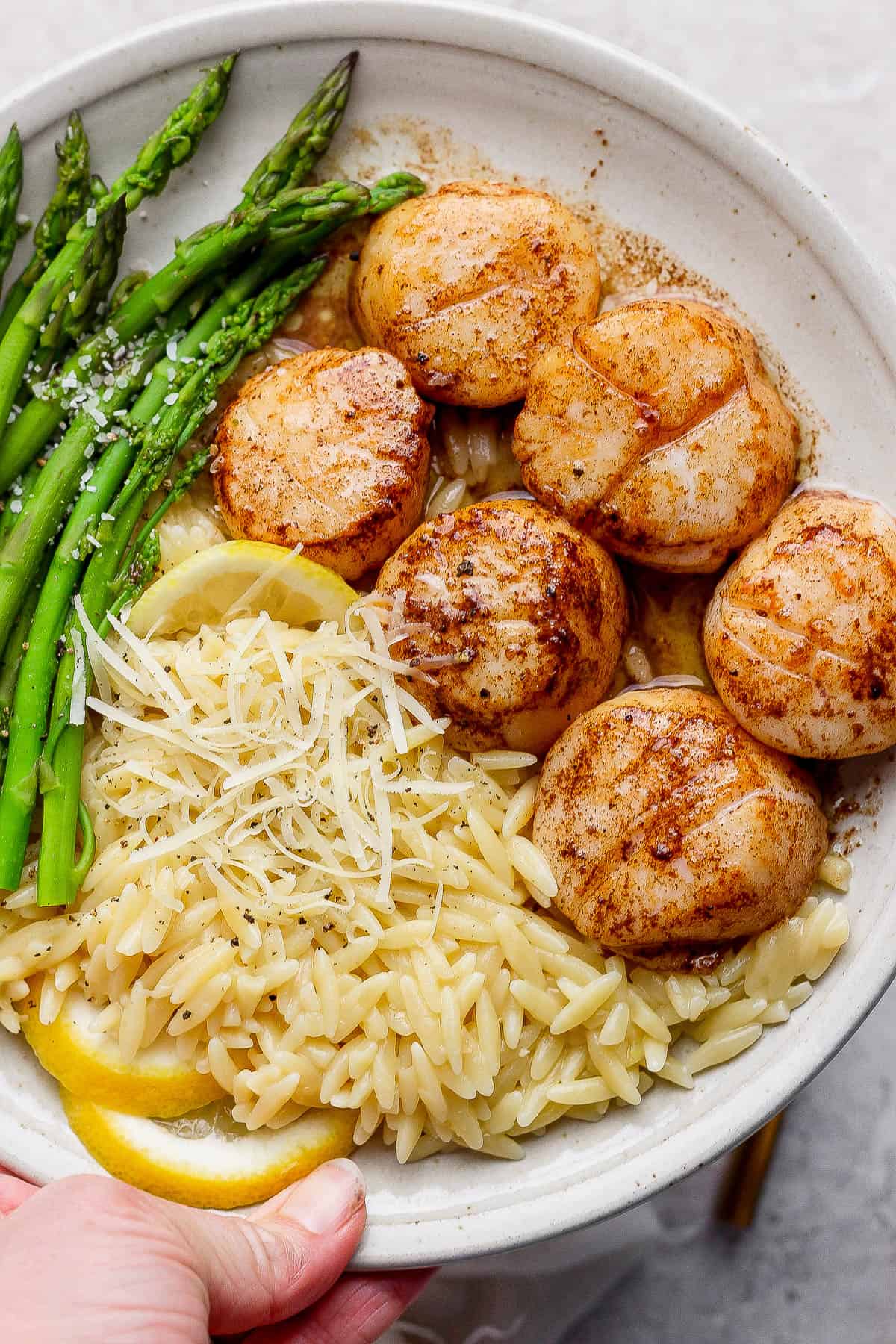 Brown butter scallops on a plate with lemon orzo, steamed asparagus, and lemon slices.