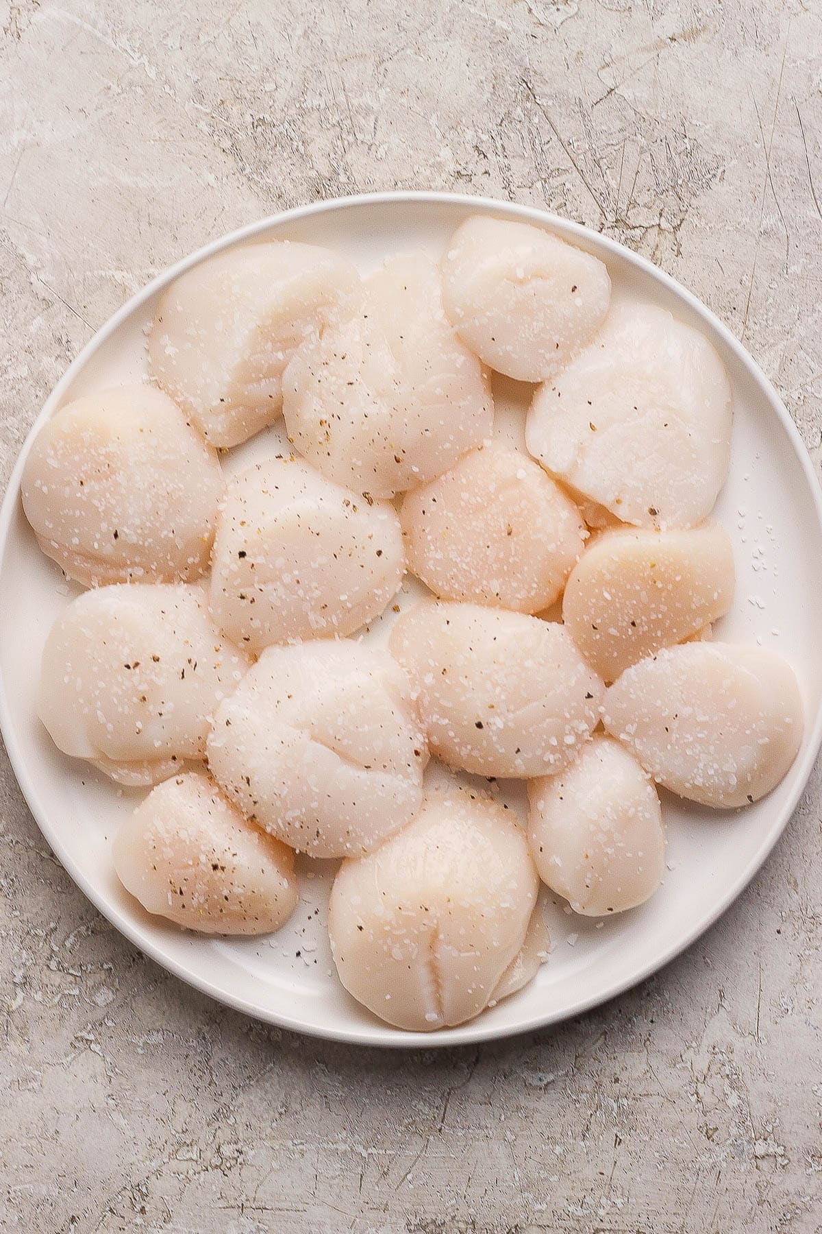Scallops seasoned with salt and pepper on a white plate.
