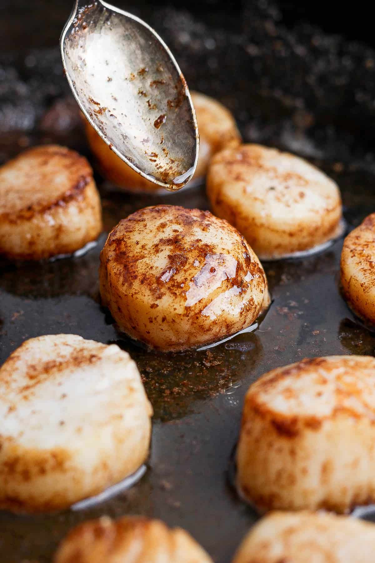 A spoon drizzling browned butter over a scallop in a skillet.