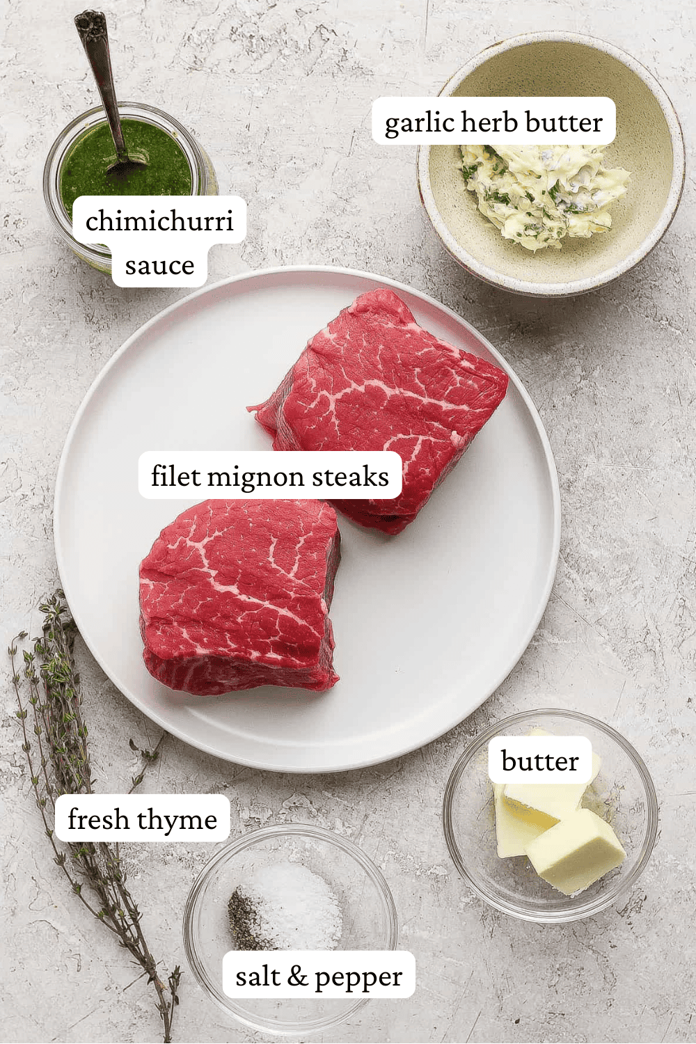 Two steaks on a plate next to bowls of chimichurri sauce, garlic herb butter, salt & pepper, fresh thyme, and regular butter with labels.