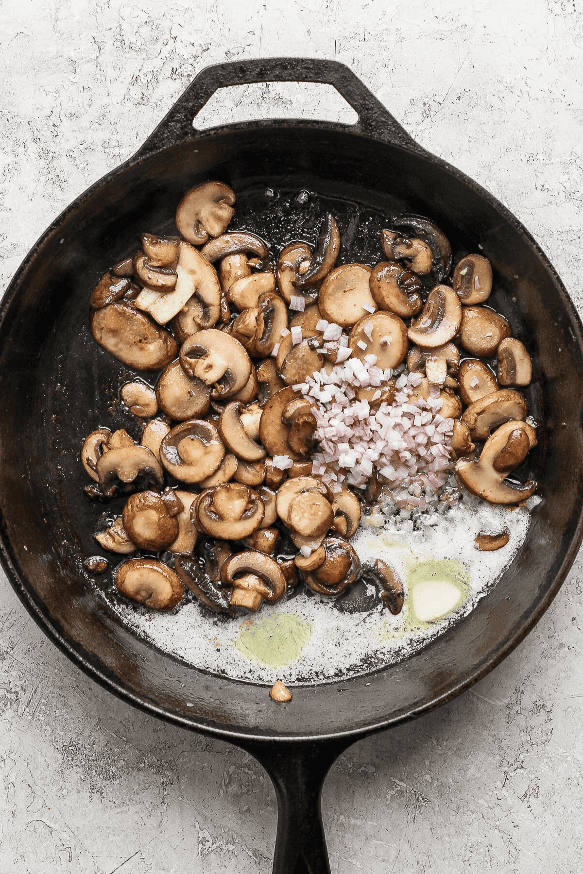Mushrooms being sauteed in butter with shallots and garlic added to them.