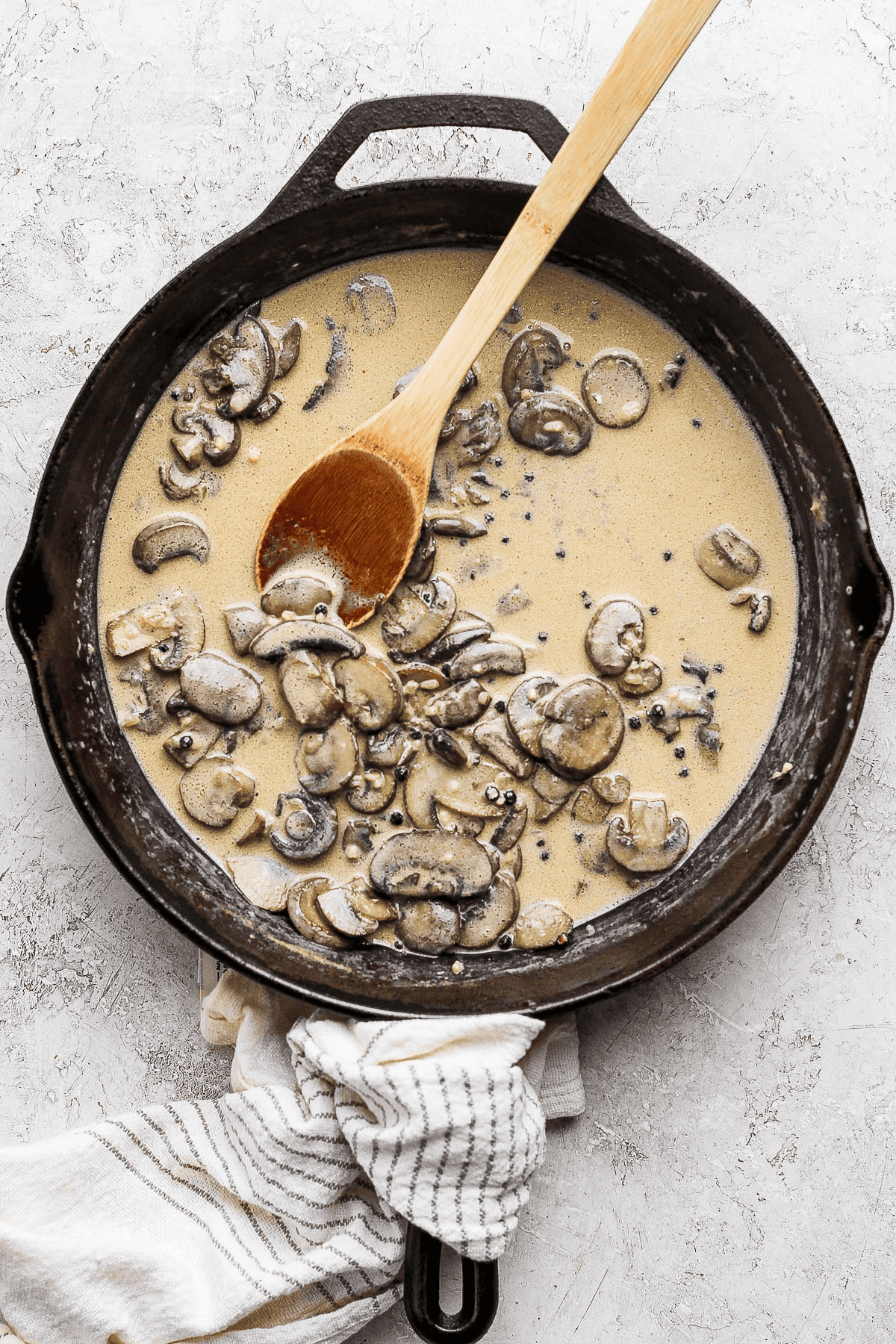 Creamy mushroom sauce in a large skillet with a wooden spoon sticking out the side.