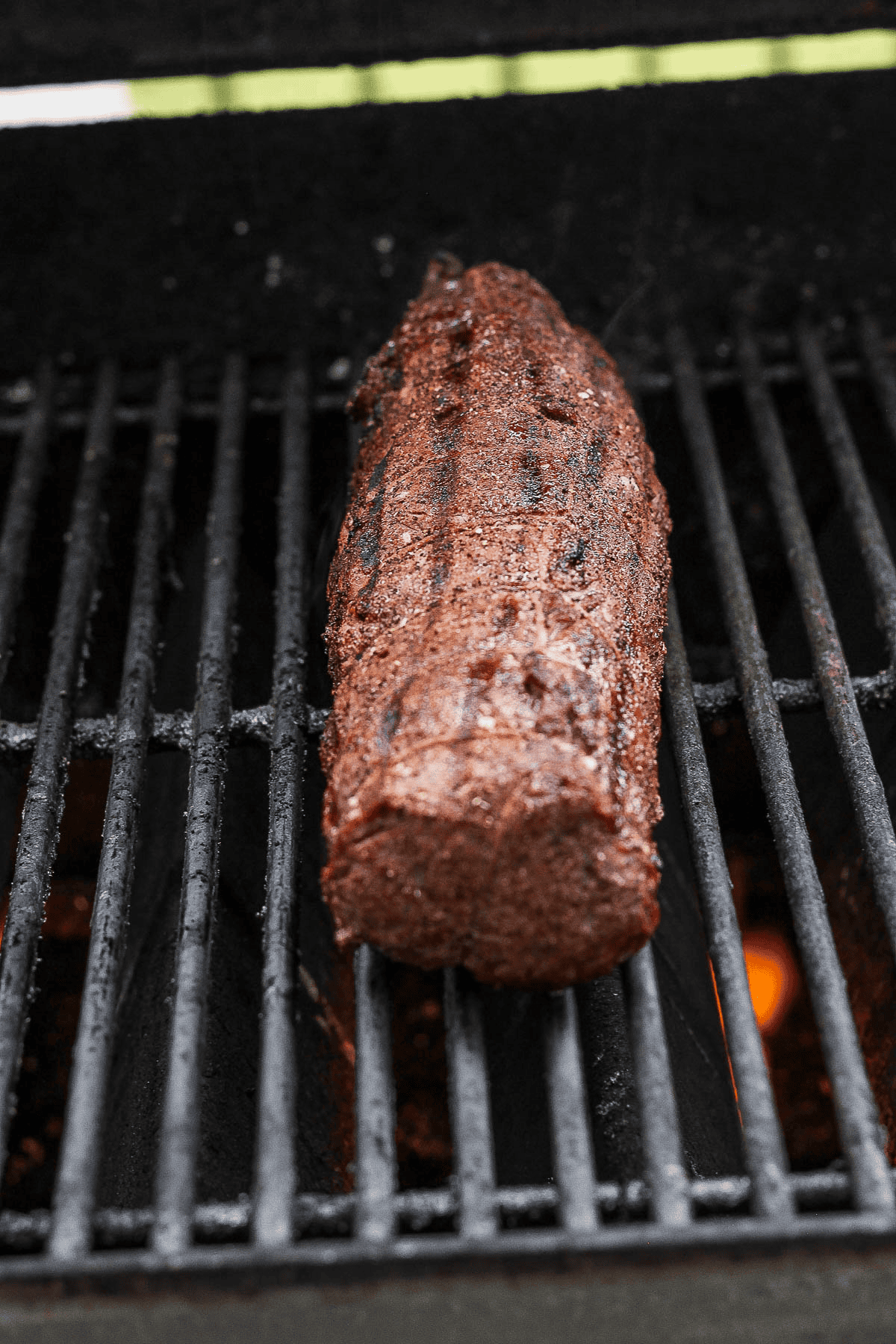 A seared beef tenderloin cooking over indirect heat on the grill.