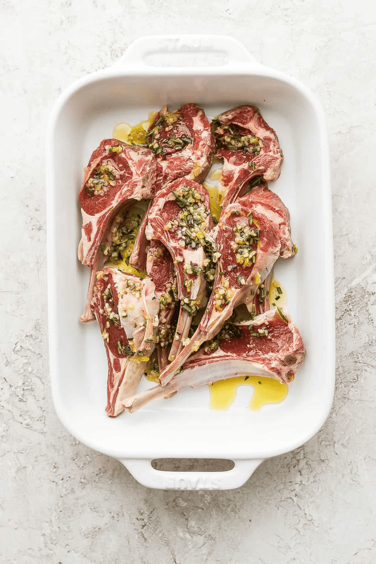 Lamb chops covered in lamb chop marinade in a white baking dish.