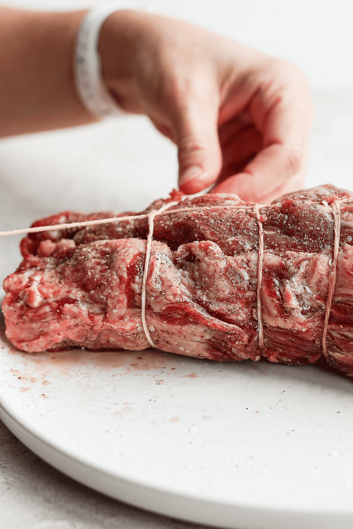 A hand securing a knot around a beef tenderloin.