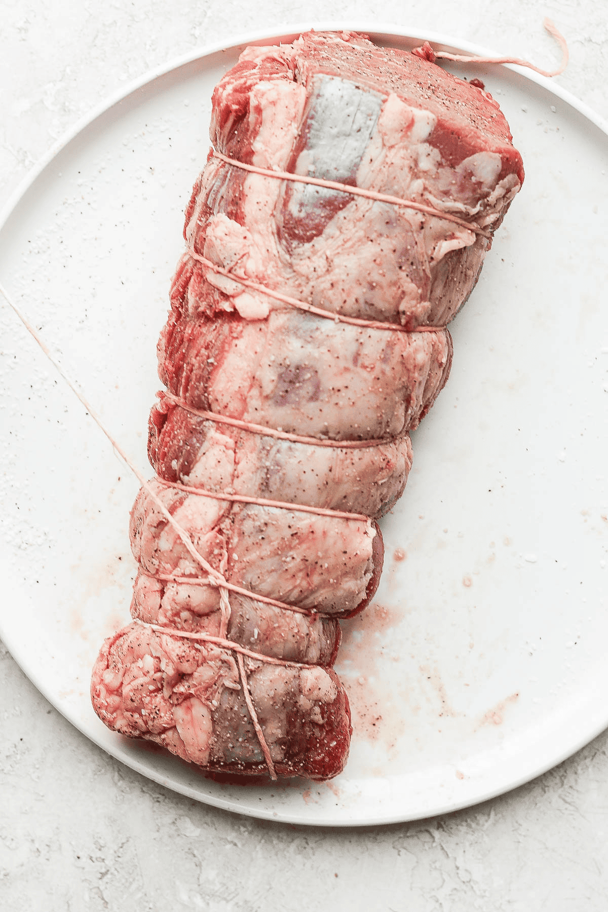 A beef tenderloin that has been tied and the twine is being wrapped down the back side.