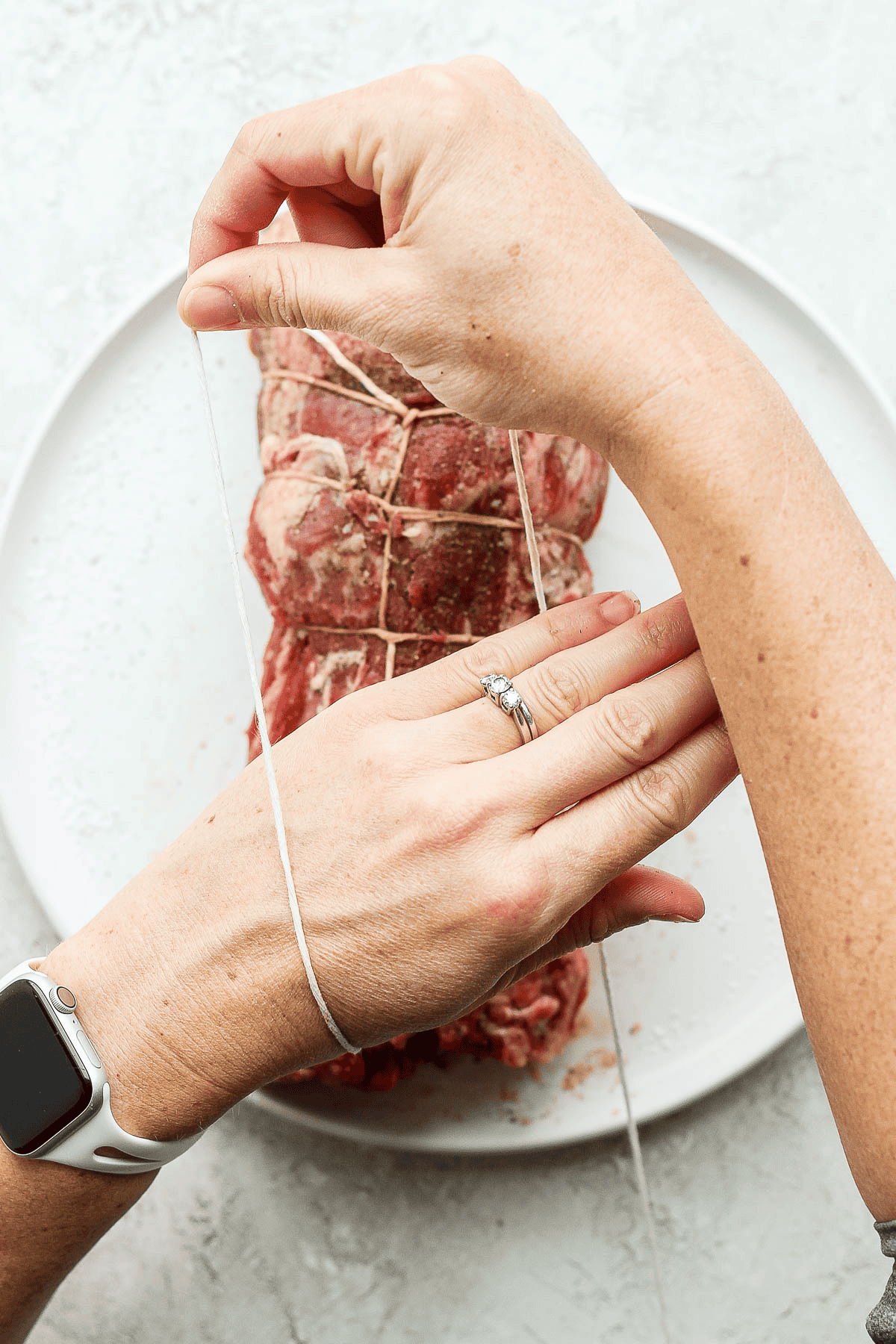 A pulling twine over a wrist that is hovering over a beef tenderloin.