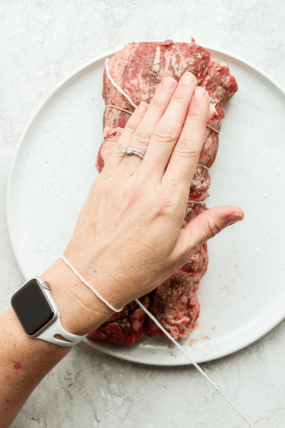Kitchen twine wrapped around someone's wrist which is hovering over a beef tenderloin.