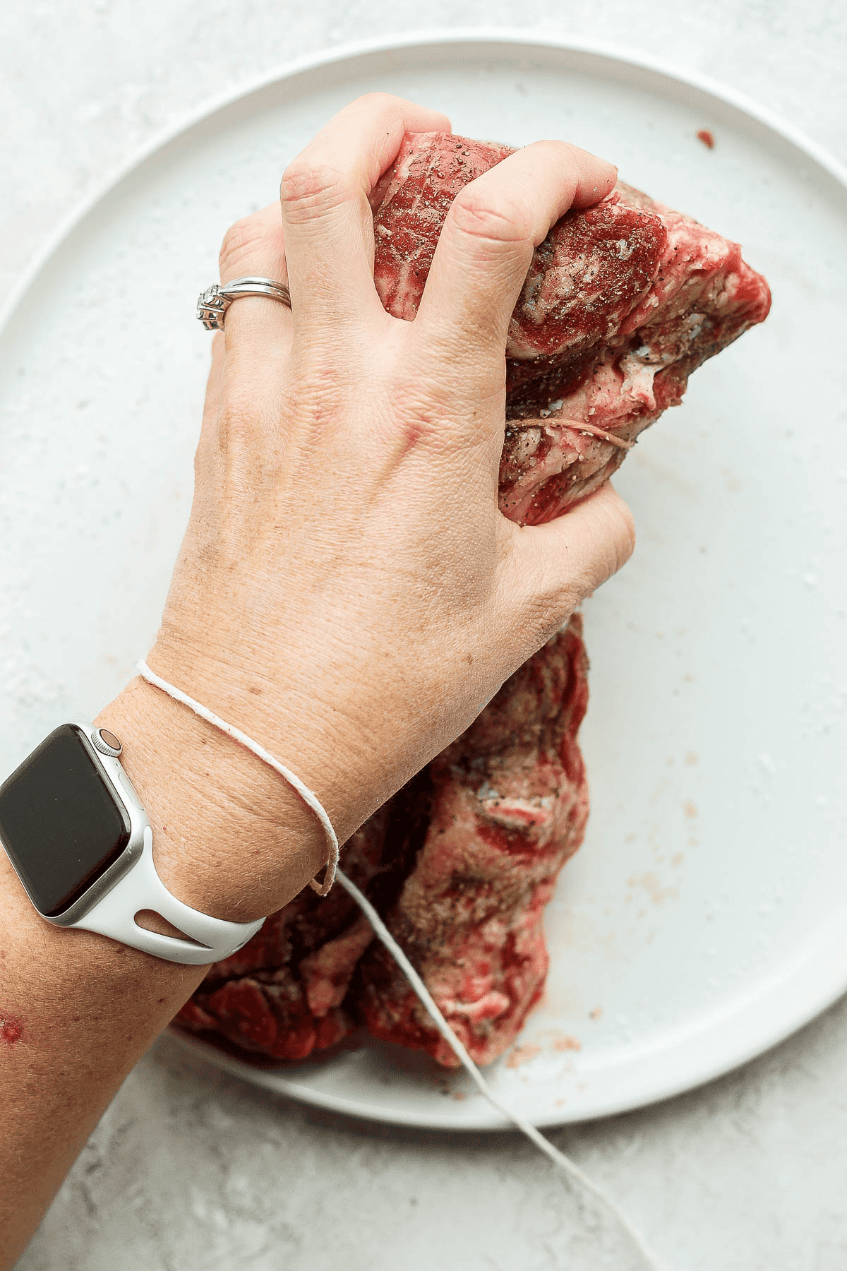A hand with twine wrapped around it grabbing one end of a beef tenderloin.