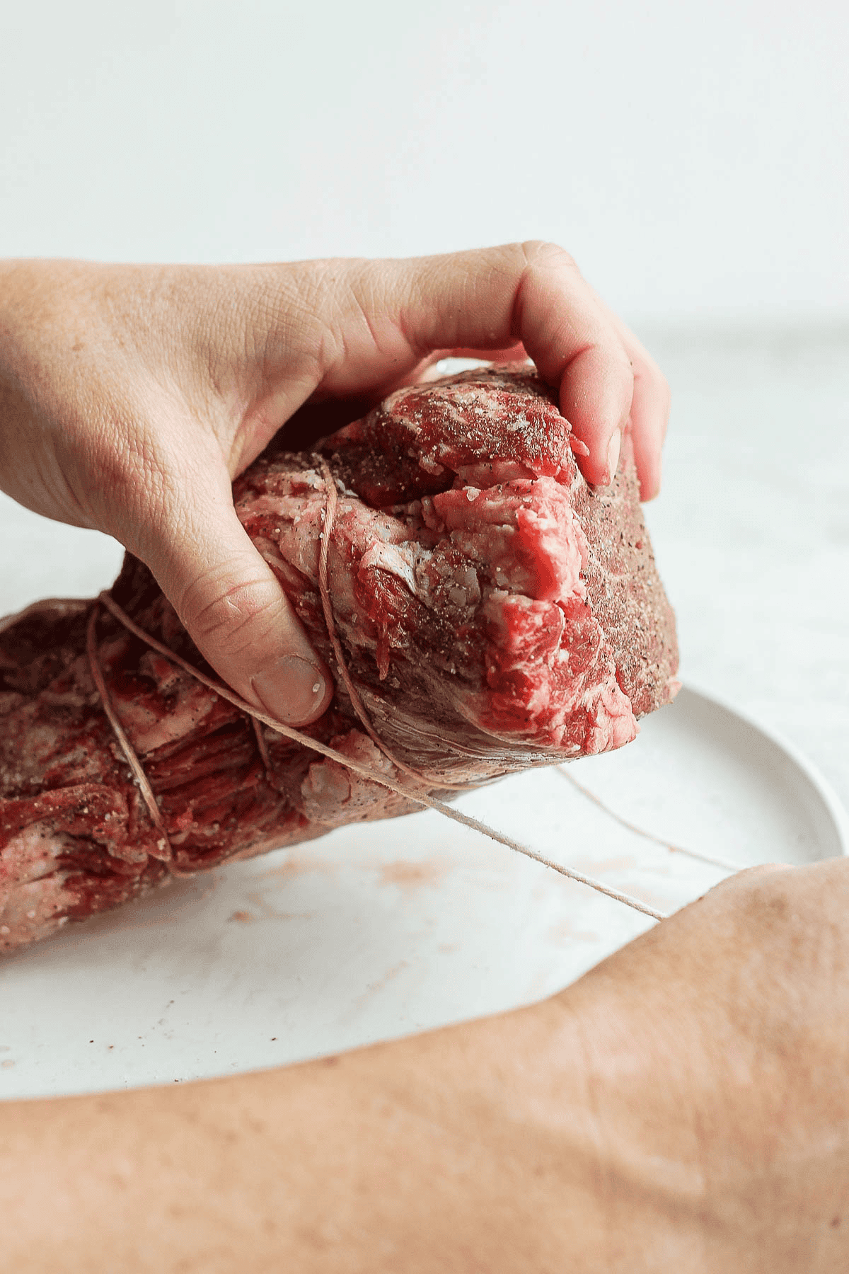 A piece of twine being pulled around a beef tenderloin.