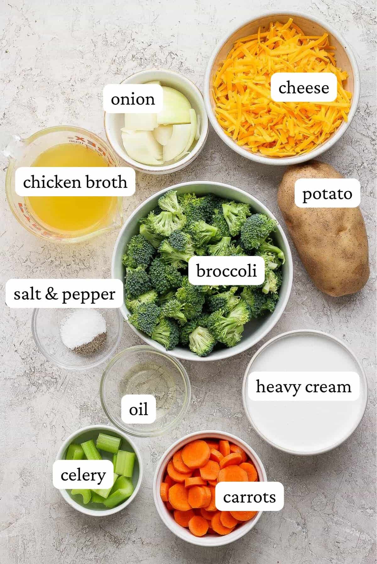Sheet pan soup ingredients including onion, shredded cheese, broccoli florets, potato, salt and pepper, oil, celery, sliced carrots, and heavy cream.