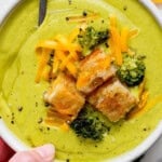 A hand holding a bowl of sheet pan soup in a bowl topped with grilled cheese croutons.