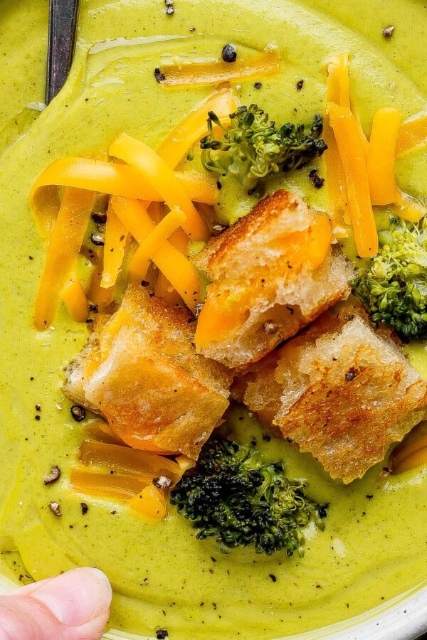 A hand holding a bowl of sheet pan soup in a bowl topped with grilled cheese croutons.