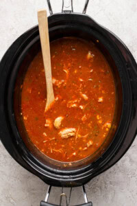 Chicken enchilada soup in a slow cooker with a wooden spoon.