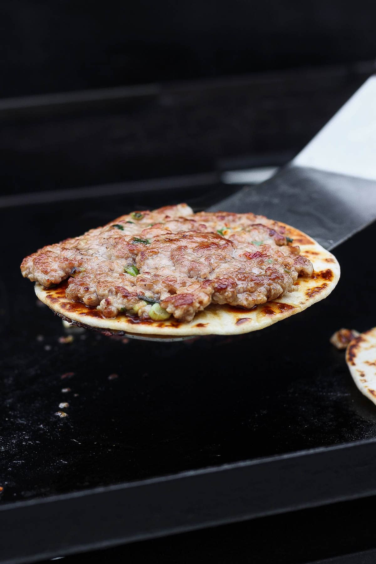 A large spatula removing a smash dumpling taco from the Blackstone.