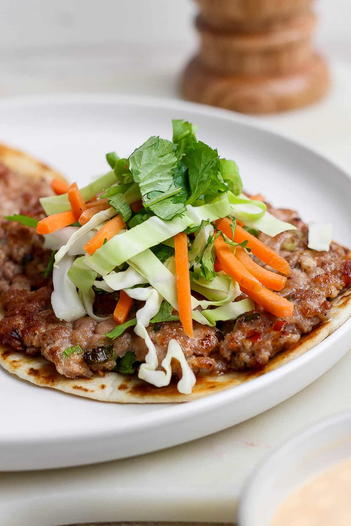 A smash dumpling taco on a white plate with some cabbage slaw added on top.