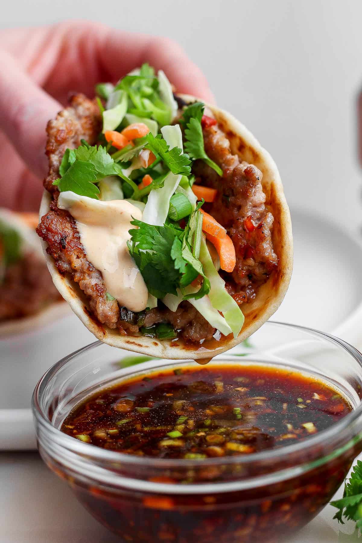 A smash dumpling taco being dipped in the dipping sauce.