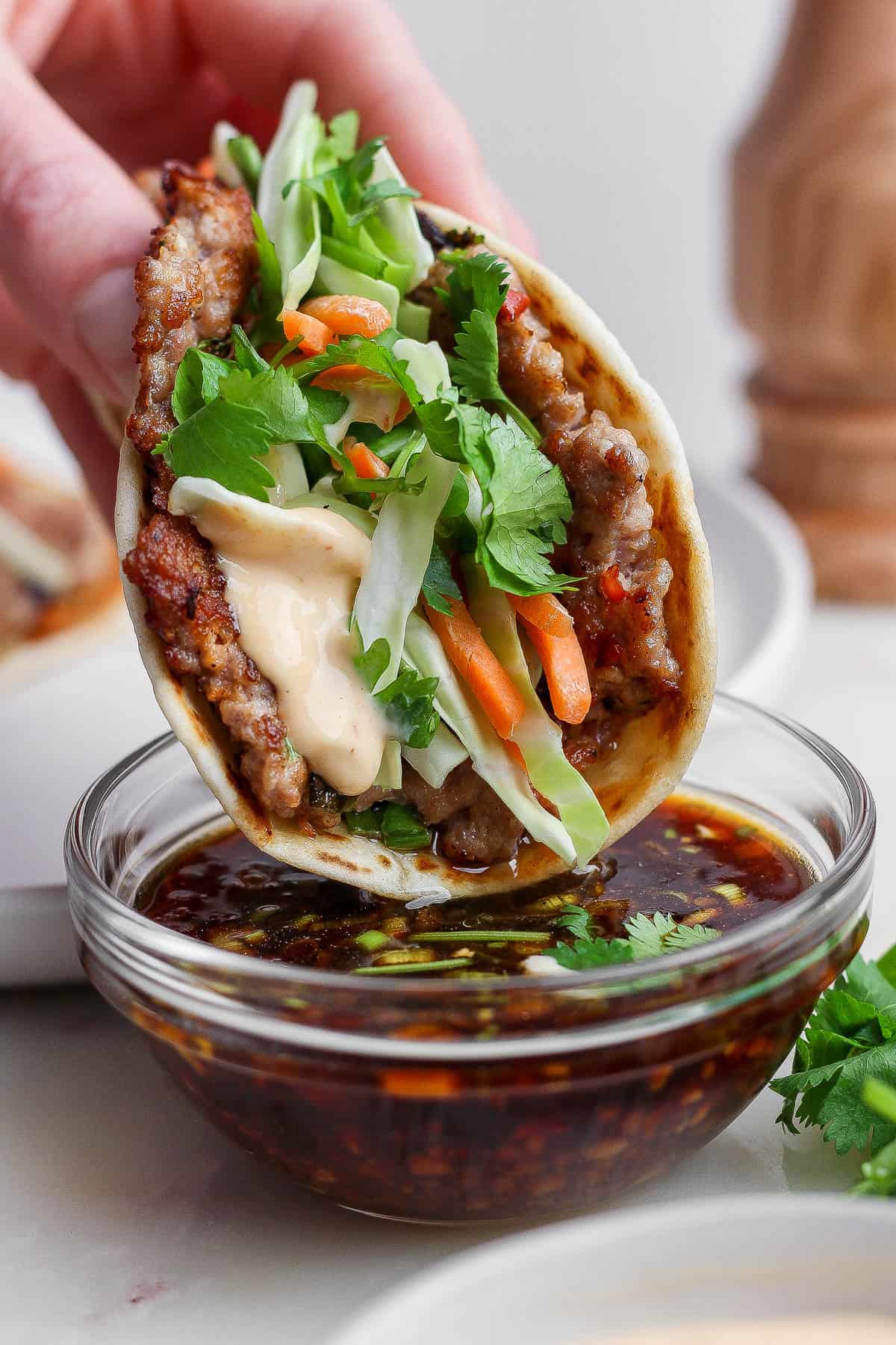 A fully assembled smash dumpling taco being dipped in the dipping sauce.