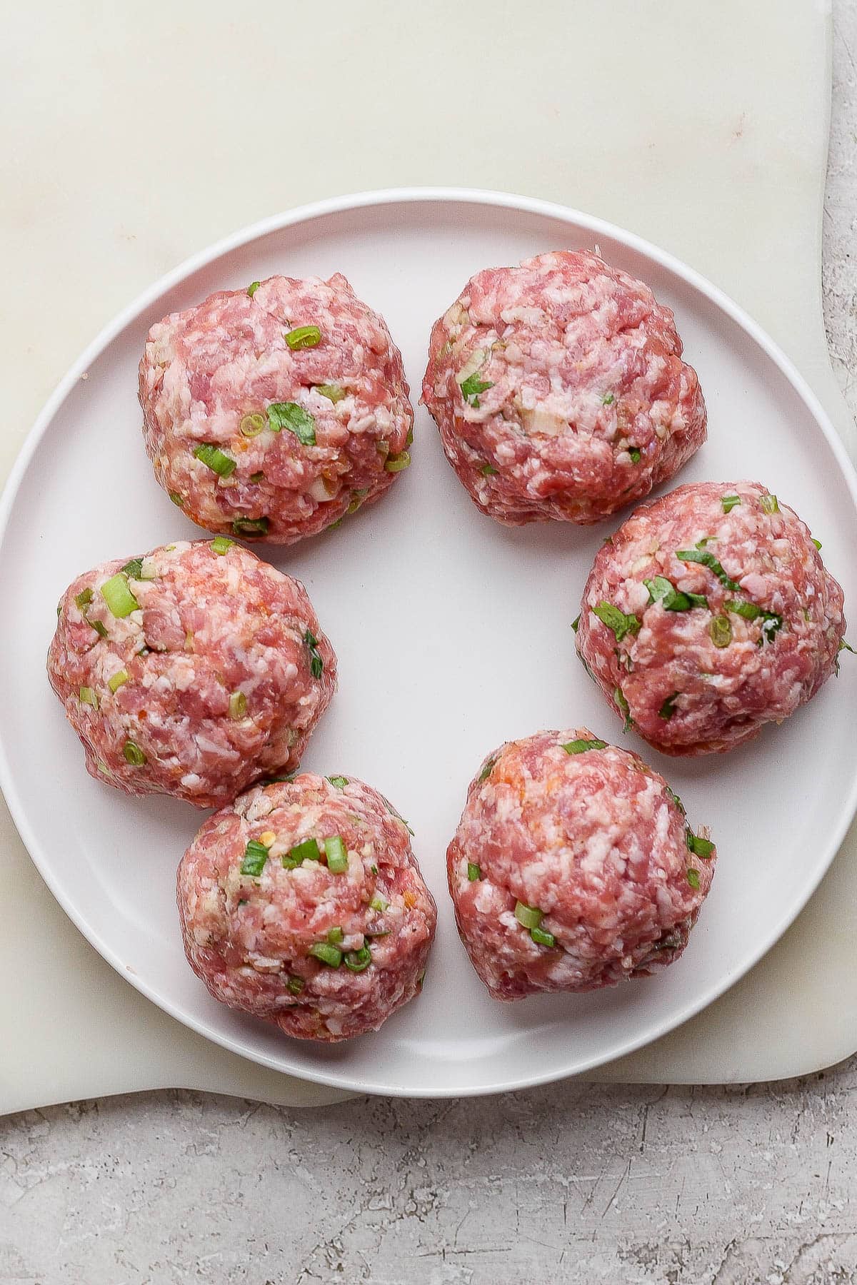 The pork mixture for smash dumpling tacos divided into six balls on a white plate.