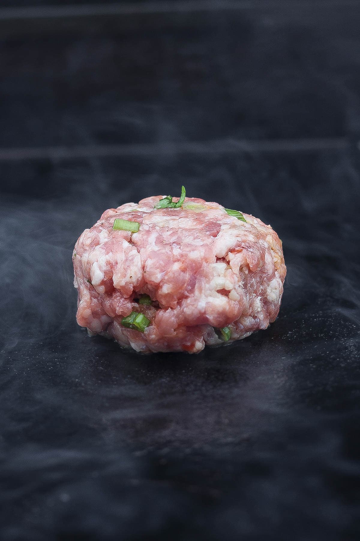 One pork ball for smash dumpling tacos on a hot Blackstone cooktop.