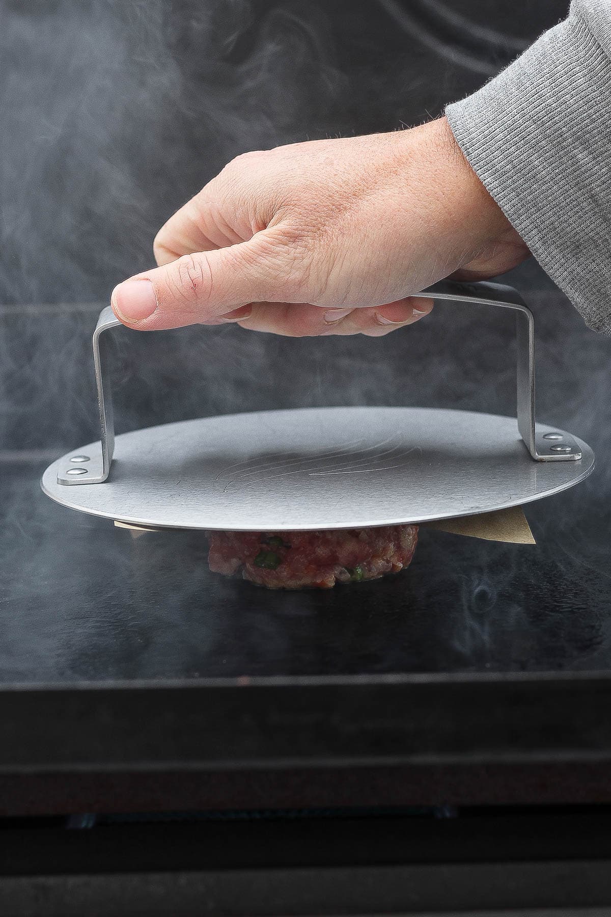 A pork ball being smashed with a burger press and parchment paper on top of it.