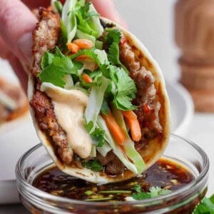 A smash dumpling taco being dipped in a small bowl of the dipping sauce.