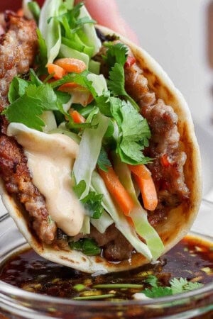 A smash dumpling taco being dipped in a small bowl of the dipping sauce.