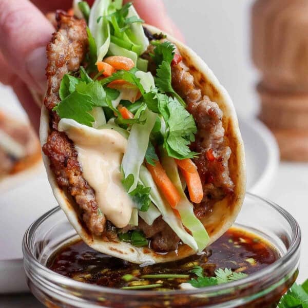 A smash dumpling taco being dipped in a small bowl of the dipping sauce.