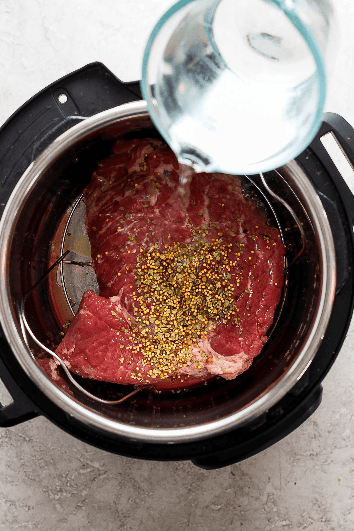 Water being poured into an Instant Pot with a trivet, corned beef brisket, and seasoning inside.