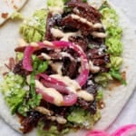 A beef short rib taco on a tortilla with smashed avocado, pickled red onions and feta cheese.