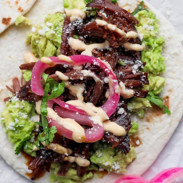 A beef short rib taco on a tortilla with smashed avocado, pickled red onions and feta cheese.