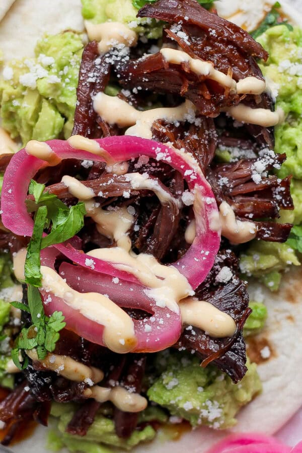 A beef short rib taco on a tortilla with smashed avocado, pickled red onions and feta cheese.