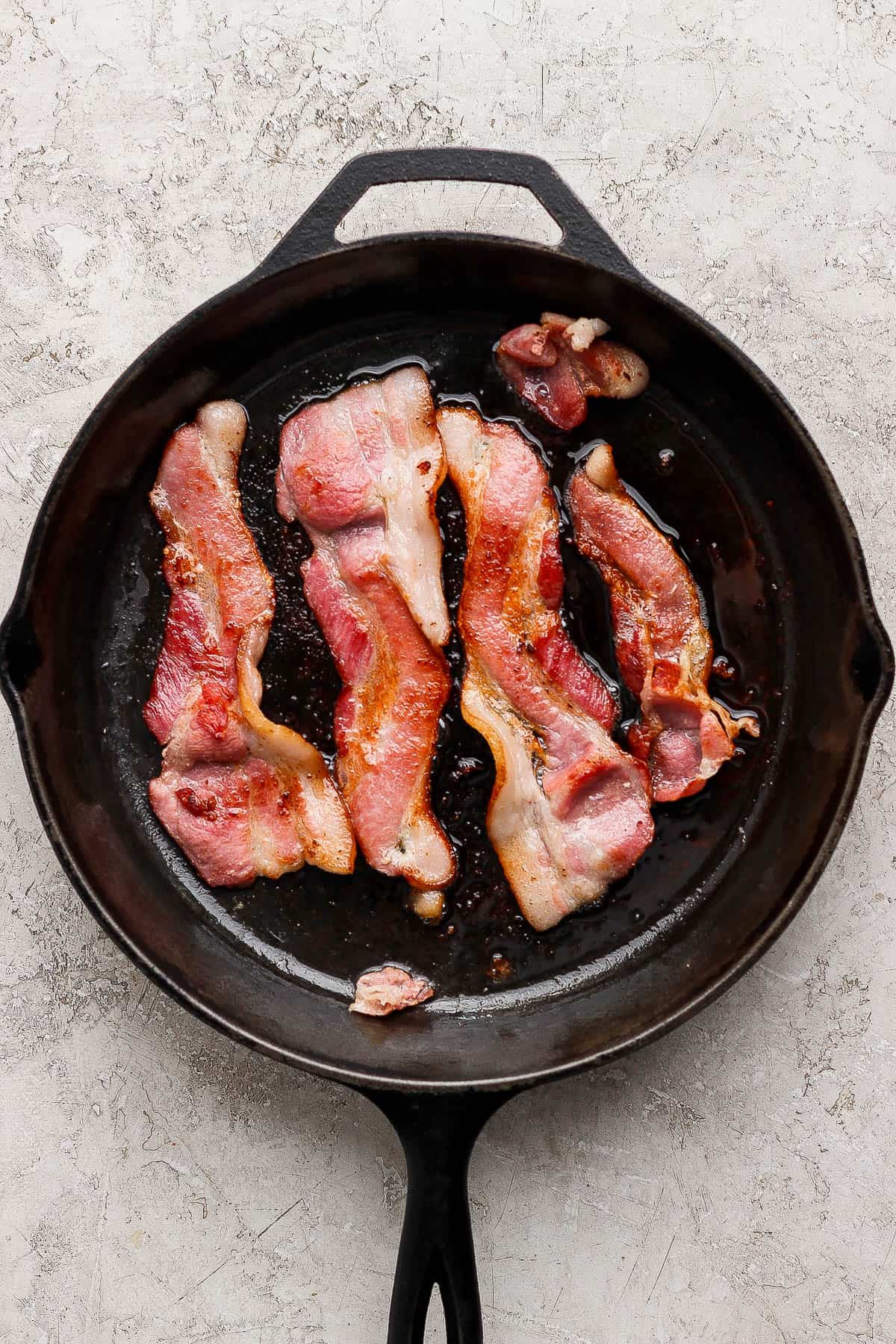 Slices of bacon being cooked in a cast iron skillet for breakfast salad.