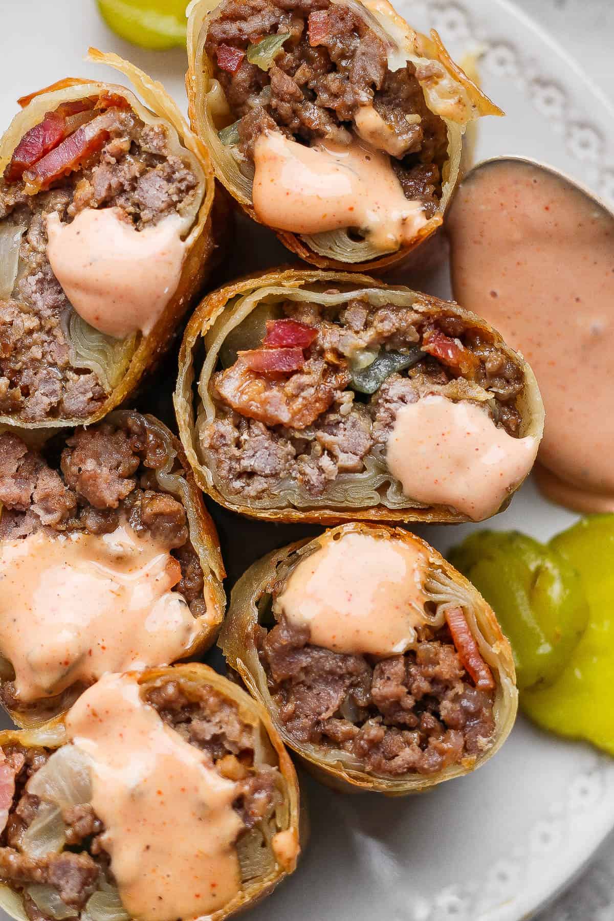 Several cheeseburger egg rolls cut in half with a little burger sauce on them.