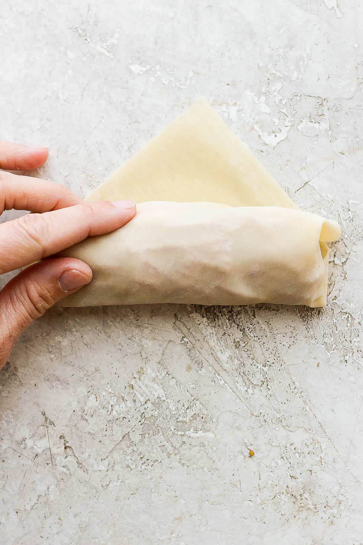 A hand holding an almost completely wrapped cheeseburger egg roll.