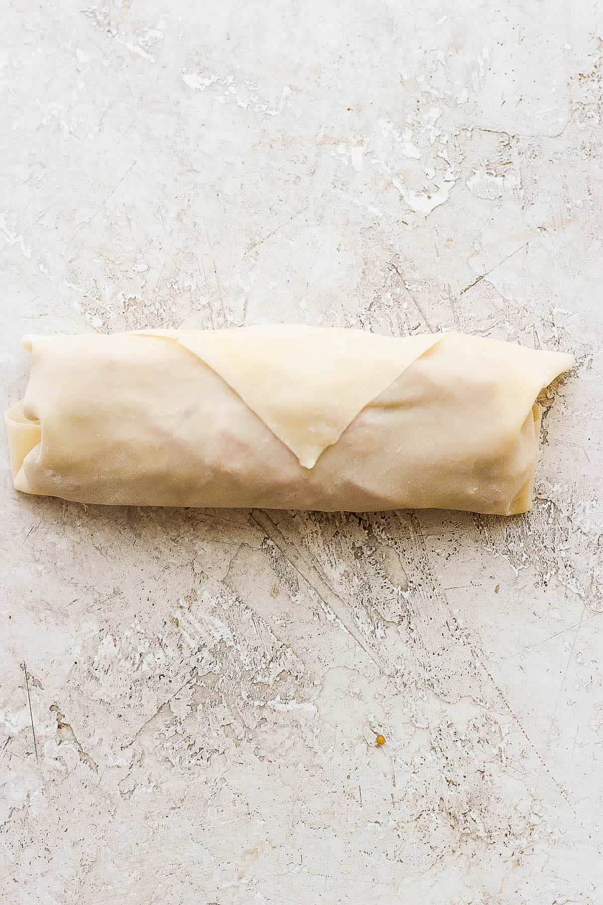 A completely wrapped cheeseburger egg roll on a counter.