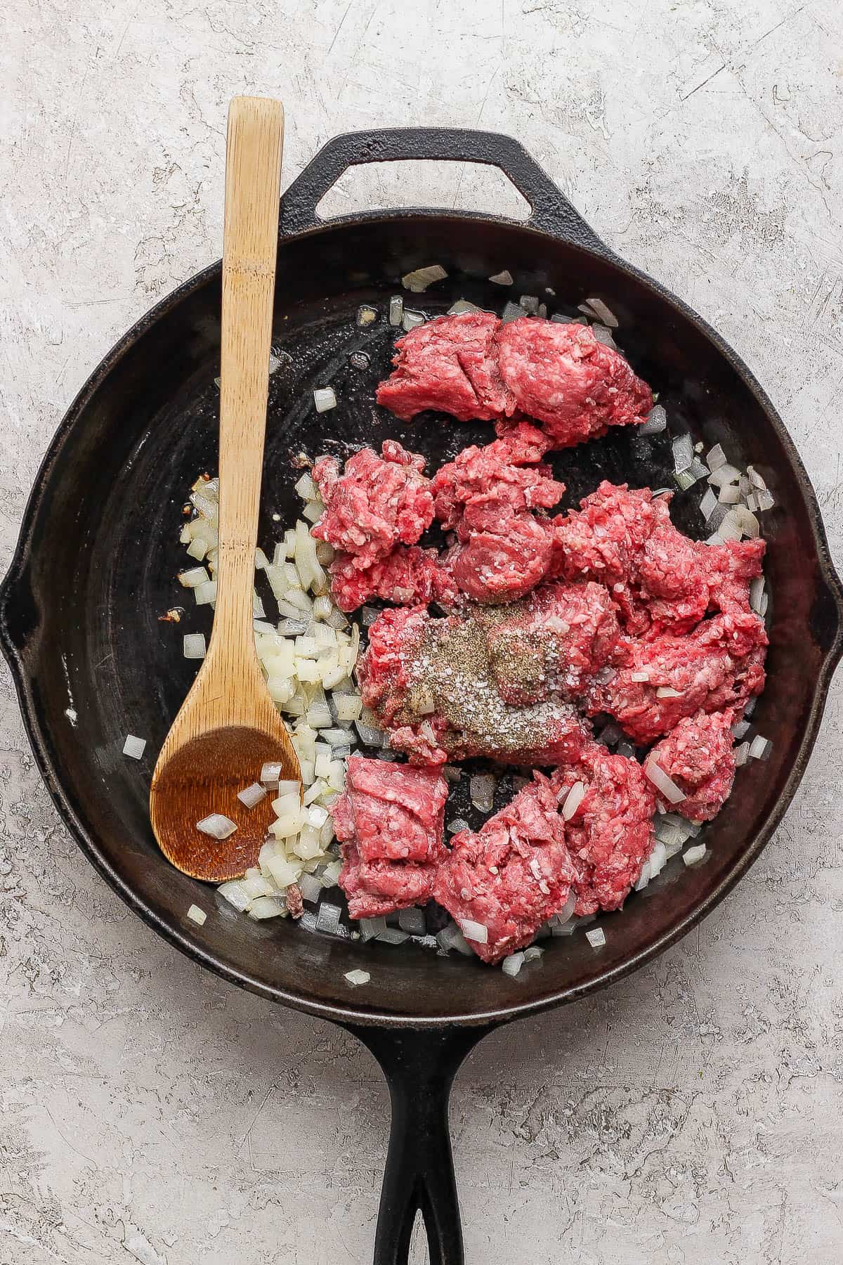Ground beef, onion, and seasonings in a cast iron skillet to make cheeseburger egg rolls.