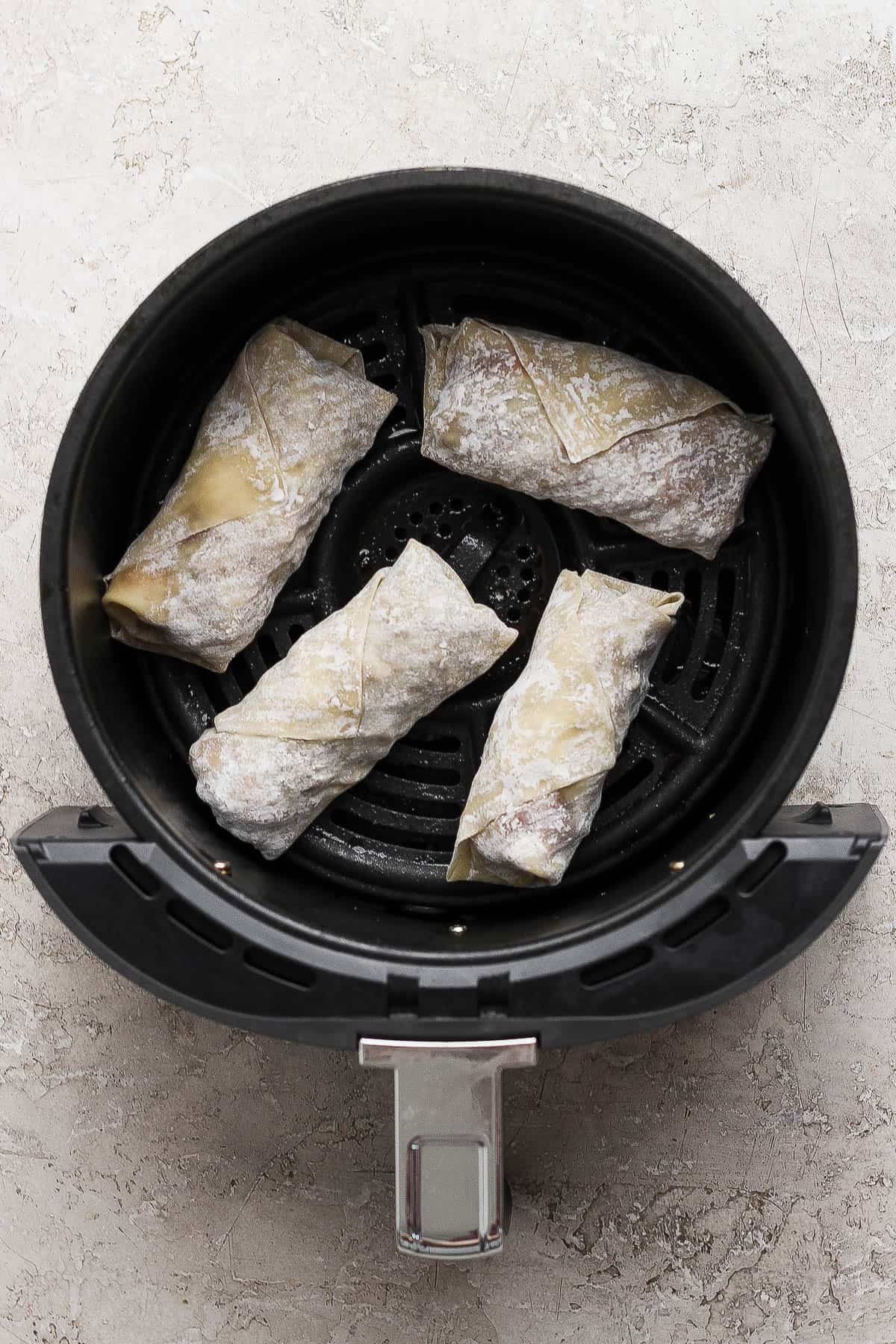 Four un-cooked cheeseburger egg rolls in an air fryer.