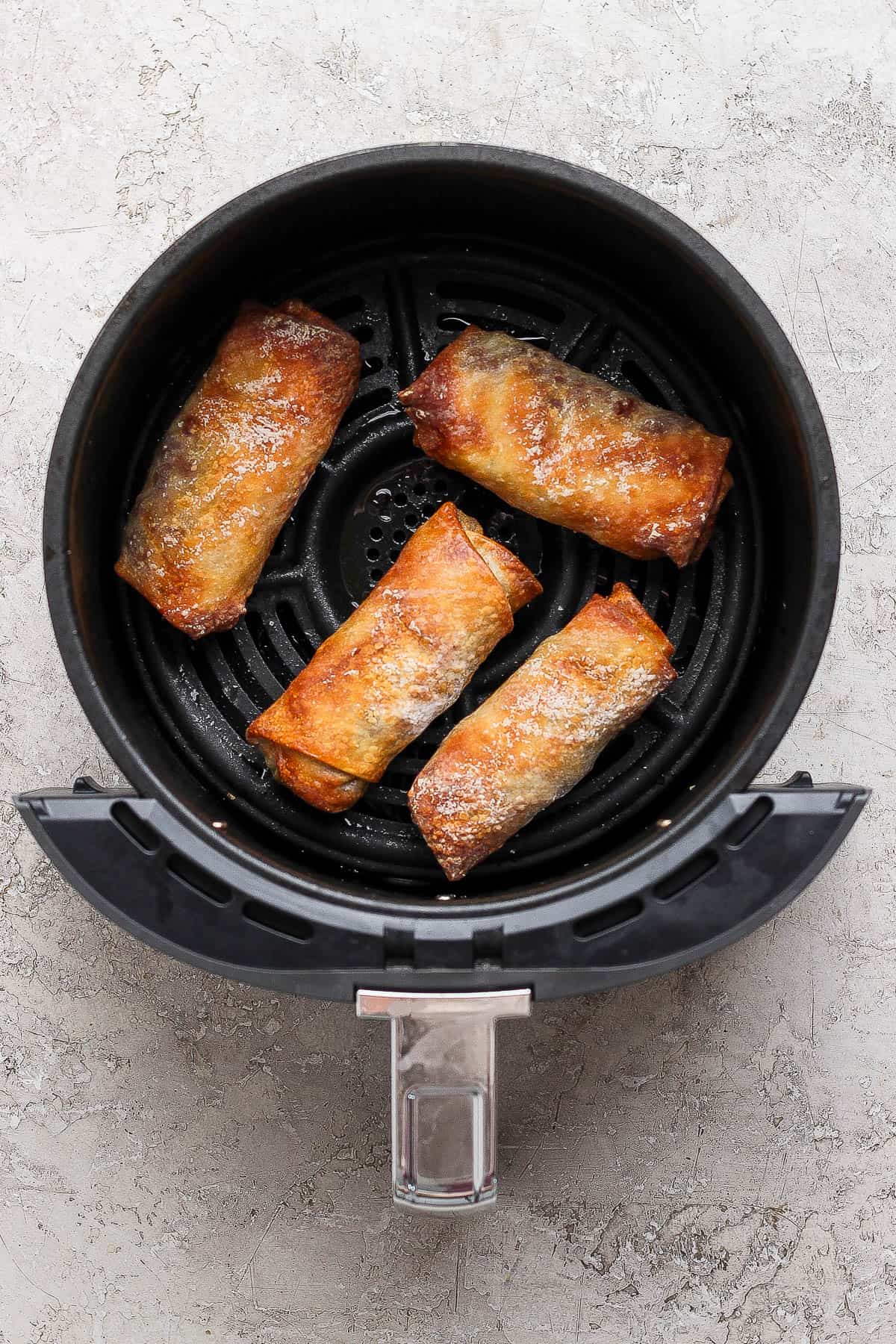Four cooked cheeseburger egg rolls in an air fryer.