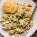 Chicken pot pie orzo on a white plate with a biscuit and gold fork.