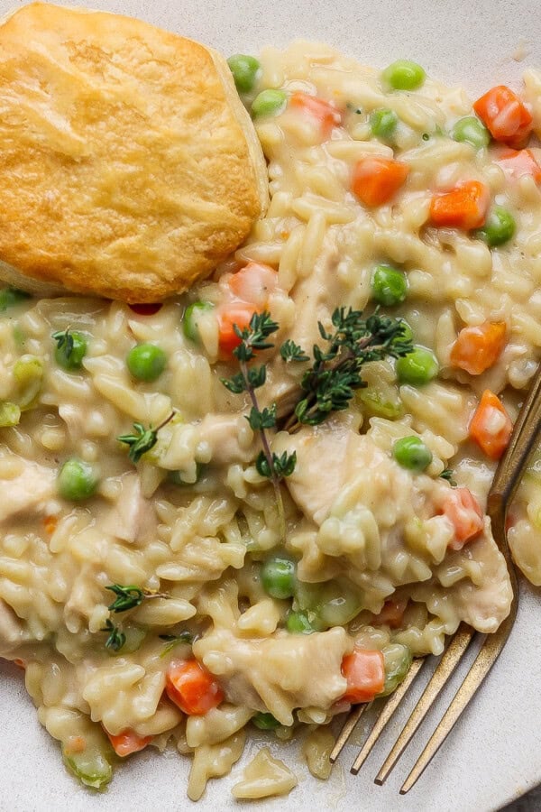 Chicken pot pie orzo on a white plate with a biscuit and gold fork.