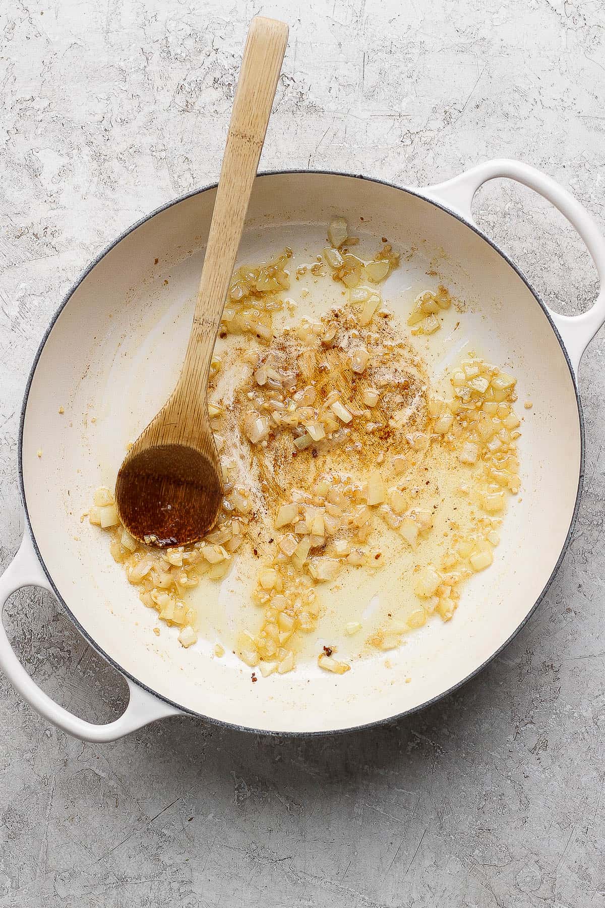 Onion and garlic sautéing in melted butter in a braising pan with a wooden spoon.
