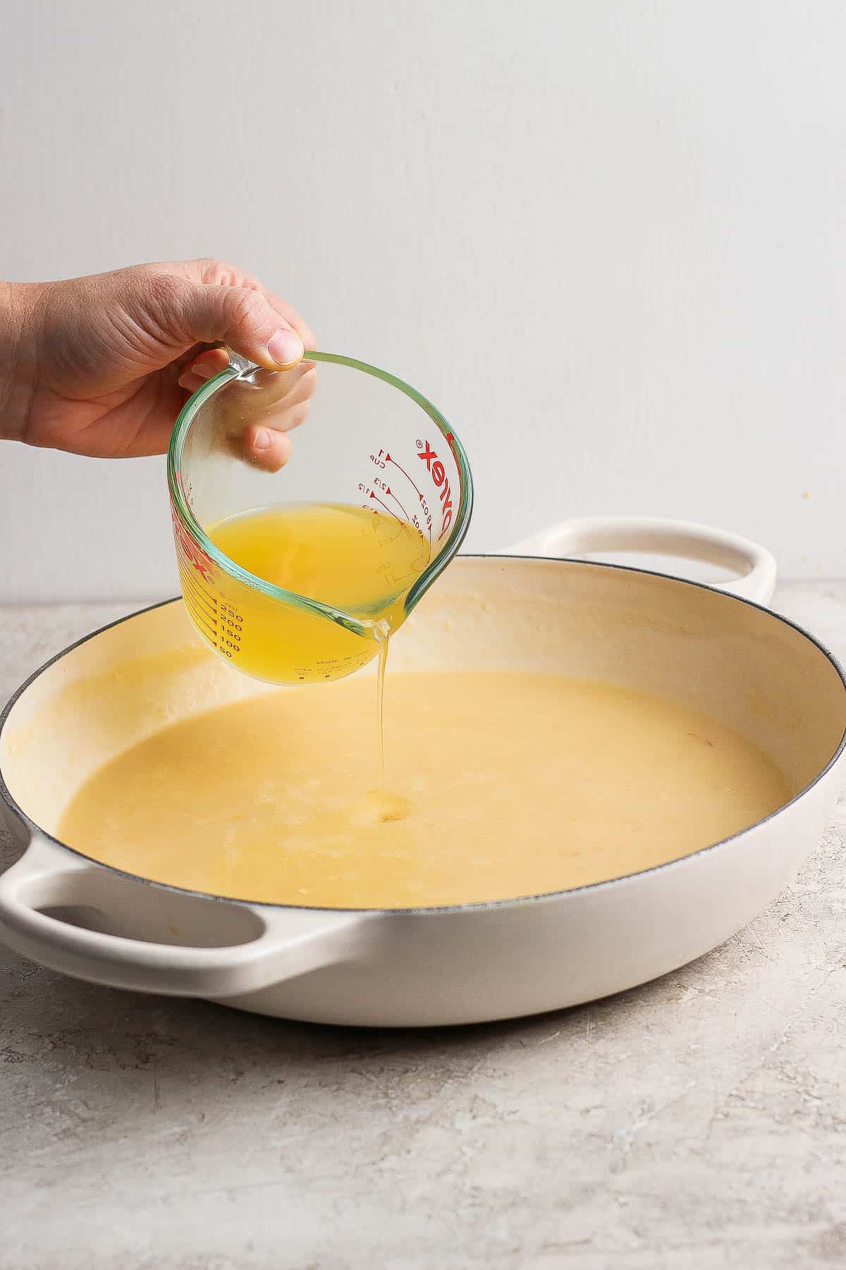 Chicken broth being poured into the roux in a braising pan.